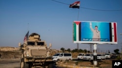 FILE - A U.S. military vehicle drives south of the northeastern city of Qamishli, on Oct. 26. 2019, as it passes by a poster showing Syrian President Bashar al-Assad. Syria’s civil entered its 14th year on March 15, 2024.