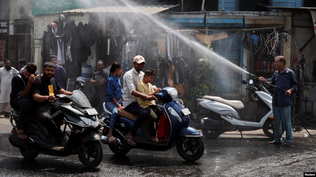 Orang-orang dengan skuter lewat di bawah alat penyiram air di bawah terik matahari pada saat musim panas di Ahmedabad, India, 9 Mei 2024. (Foto: Reuters)