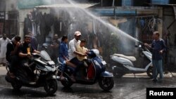 Orang-orang dengan skuter lewat di bawah alat penyiram air di bawah terik matahari pada saat musim panas di Ahmedabad, India, 9 Mei 2024. (Foto: Reuters)