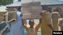 A boy in Kaduna, Nigeria, holds a sign in protest the day after the kidnapping of hundreds of students by gunmen after the Friday prayer in Kaduna, Nigeria, March 8, 2024.