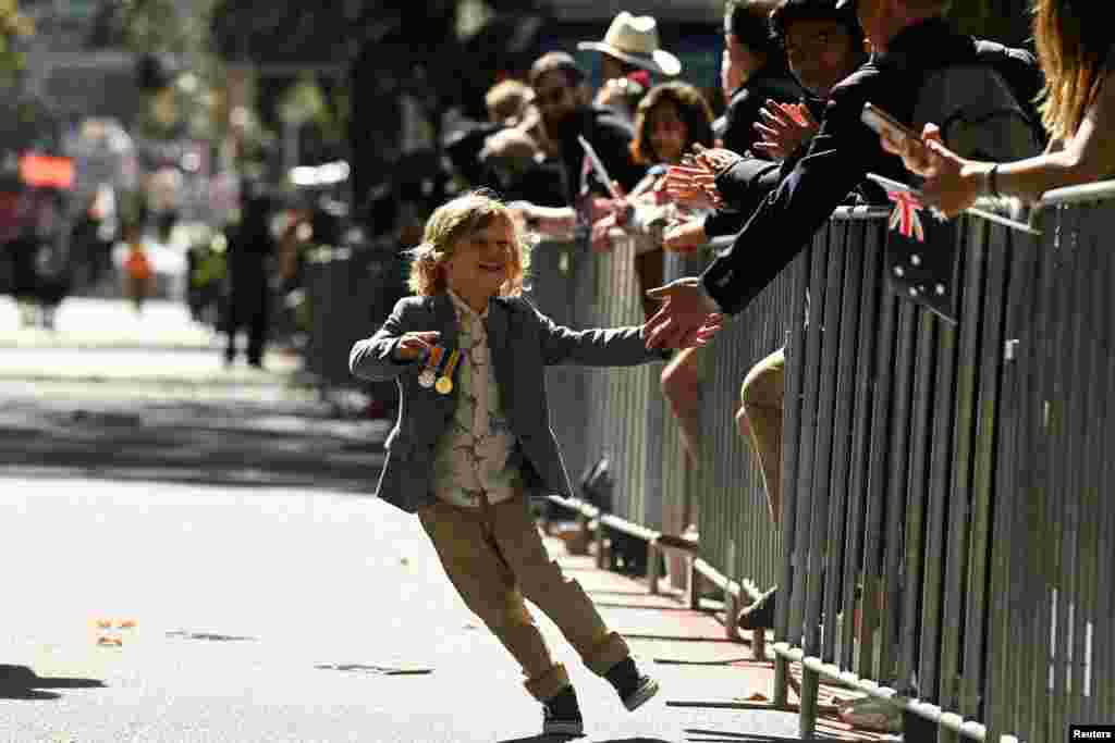 A young marcher high fives the crowd as Australian military personnel, past and present, commemorate ANZAC Day during a parade through the city center in Sydney.