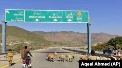 FILE - A motorcyclist drives past sheep on a newly built road in Haripur, Pakistan, on Dec. 22, 2017. China launched the Belt and Road Initiative in 2013 to expand its trade and influence by building roads, ports and other infrastructure overseas. (AP Photo/Aqeel Ahmed, File)