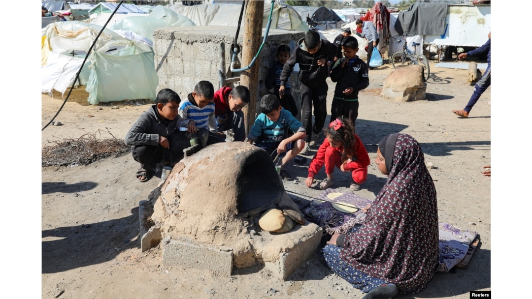 Palestinka peče hleb dok deca sede oko nje, dok se stanovnici Gaze suočavaju sa krizom gladi, u Kan Junisu, na jugu Pojasa Gaze, 24. januara 2024.