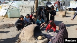A Palestinian woman bakes bread as children sit next to her, while Gaza residents face crisis levels of hunger and soaring malnutrition, in Khan Younis in the southern Gaza Strip, Jan. 24, 2024.