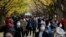 FILE - People wearing protective masks take photos as they walk through the row of ginkgo trees along a sidewalk as the trees and sidewalk are covered with the bright yellow leaves at Jingu Gaien park area on Nov. 28, 2020, in Tokyo. 