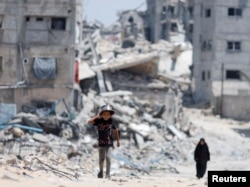 Warga Palestina berjalan melewati rumah-rumah yang hancur akibat serangan Israel, di tengah konflik yang sedang berlangsung antara Israel dan Hamas, di Khan Younis, di selatan Jalur Gaza, 22 Mei 2024. (Foto: REUTERS/Mohammed Salem)