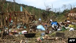 Orang-orang melihat puing-puing setelah serangan militer di sebuah kamp pengungsi di dekat Kota Laiza di Myanmar utara pada 11 Oktober 2023, dua hari setelah serangan yang menewaskan 29 orang dan melukai puluhan lainnya. (Foto: AFP)