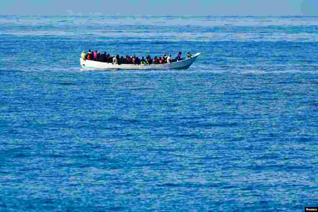 A wooden boat carrying migrants waits to be rescued by a Spanish coast guard vessel, near Bahia Feliz Beach, in the island of Gran Canaria, Spain.