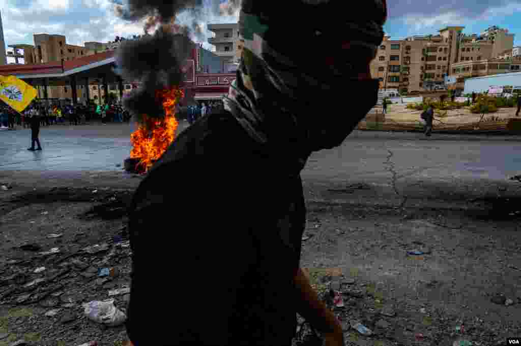 A young Palestinian walks by tires set on fire during a protest on the outskirts of Ramallah, Oct. 20, 2023. (Yan Boechat/VOA)