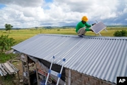Antonius Makambombu, a worker of Sumba Sustainable Solutions performs maintenance work on a solar panel on the roof of a customer's shop in Laindeha village on Sumba Island, Indonesia, Wednesday, March 22, 2023. (AP Photo/Dita Alangkara)