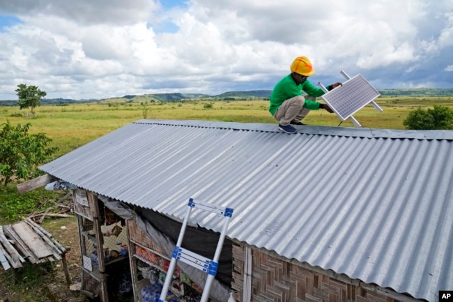 Antonius Makambombu, a worker of Sumba Sustainable Solutions performs maintenance work on a solar panel on the roof of a customer's shop in Laindeha village on Sumba Island, Indonesia, Wednesday, March 22, 2023. (AP Photo/Dita Alangkara)