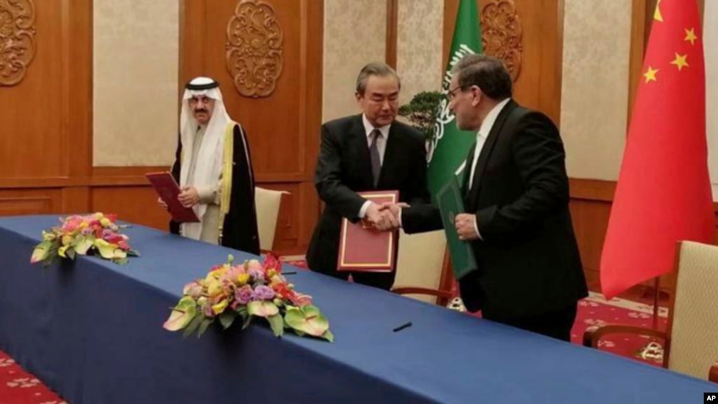 Iranian security council official Ali Shamkhani shakes hands with China's senior foreign policy official Wang Yi as Saudi security adviser Musaad bin Mohammed al-Aiban watches during a signing of an accord to reset Iranian-Saudi ties, in Beijing, March 10, 2023. (Nournews via AP)