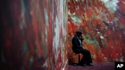 A guard sits by a painting in an exhibition on Leon Monet at the Musée du Luxembourg in Paris, Monday, March 13, 2023. (AP Photo/Lewis Joly)