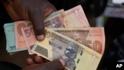 FILE - A currency trader holds worthless Zimbabwean dollar notes on the streets of Harare, Zimbabwe, June, 9, 2022.