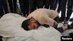 Palestinian lawyer Jehad Al-Kafarnah, whose 8-month-old stillborn and wife were killed in an Israeli strike, according to health officials, mourns over his wife's shrouded body at a hospital in the northern Gaza Strip, Oct. 27, 2023.