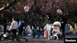 Parents push strollers with their babies in a park in Shanghai, China, April 2, 2023.
