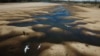 FILE - Birds fly over a man taking photos of the exposed riverbed of the Old Parana River, a tributary of the Parana River during a drought in Rosario, Argentina, July 29, 2021.