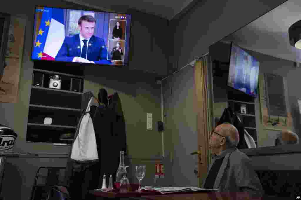 A man at a cafe watches French President Emmanuel Macron speaking during a television interview with reporters, in Marseille, France.