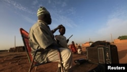 FILE - A Sudanese man listens to the radio with his family at dawn on the first day of election in Khartoum April 11, 2010. 