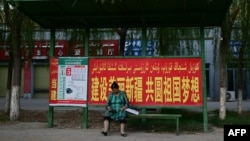 FILE - This picture taken July 17, 2023, shows a woman sitting at a bus stop bearing a government slogan to 'build a beautiful Xinjiang and nurture the motherland's dreams' in Yarkant in northwestern China's Xinjiang region.
