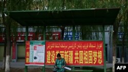 FILE - A woman sits at a bus stop bearing a government slogan to "build a beautiful Xinjiang and nurture the motherland's dreams" in Yarkant in northwestern China's Xinjiang region on July 17, 2023. 