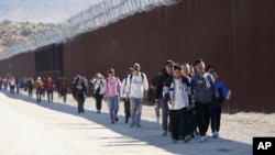 FILE - A group of people, including many from China, walk along the wall after crossing the border with Mexico to seek asylum, near Jacumba, California, Oct. 24, 2023.