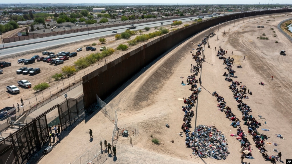 Di dân sắp hàng bên ngoài hàng rào biên giới chờ được chở đến một cơ sở của Tuần tra Biên giơi Mỹ ở El Paso, Texas, ngày 10/5/2023.