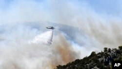 A helicopter drops water over a fire in Nea Makri, east of Athens, Aug. 12, 2024, as hundreds of firefighters tackle a major wildfire raging out of control near Athens.