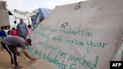 FILE—A man writes a message of thanks to students in the U.S. protesting in solidarity with the people of Gaza, on a tent at a camp for displaced Palestinians in Rafah, in the southern Gaza Strip, April 27, 2024.