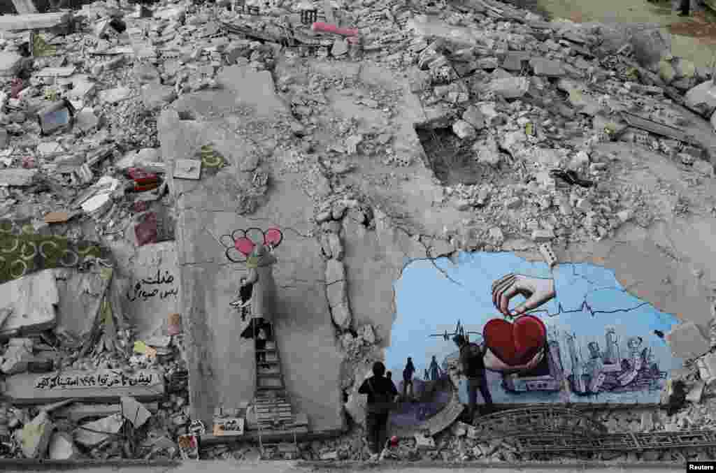 Seniman Suriah Aziz Asmar dan Salam Hamed melukis seni jalanan di atas puing-puing bangunan yang rusak setelah gempa mematikan, di kota Jandaris yang dikuasai pemberontak, Suriah.