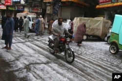 Orang-orang berjalan di jalan yang tertutup butiran hujan es di Peshawar, Pakistan, Sabtu, 30 Maret 2024. (Foto: Mohammad Sajjad/AP Photo)