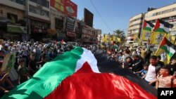 Orang-orang di Kota Nablus, di Tepi Barat yang diduduki, membentangkan bendera Palestina raksasa dalam pawai untuk menunjukkan dukungan terhadap warga di Jalur Gaza di tengah pertempuran antara Israel dan Hamas, Kamis, 26 Oktober 2023. (Foto: Zain Jaafar/AFP)