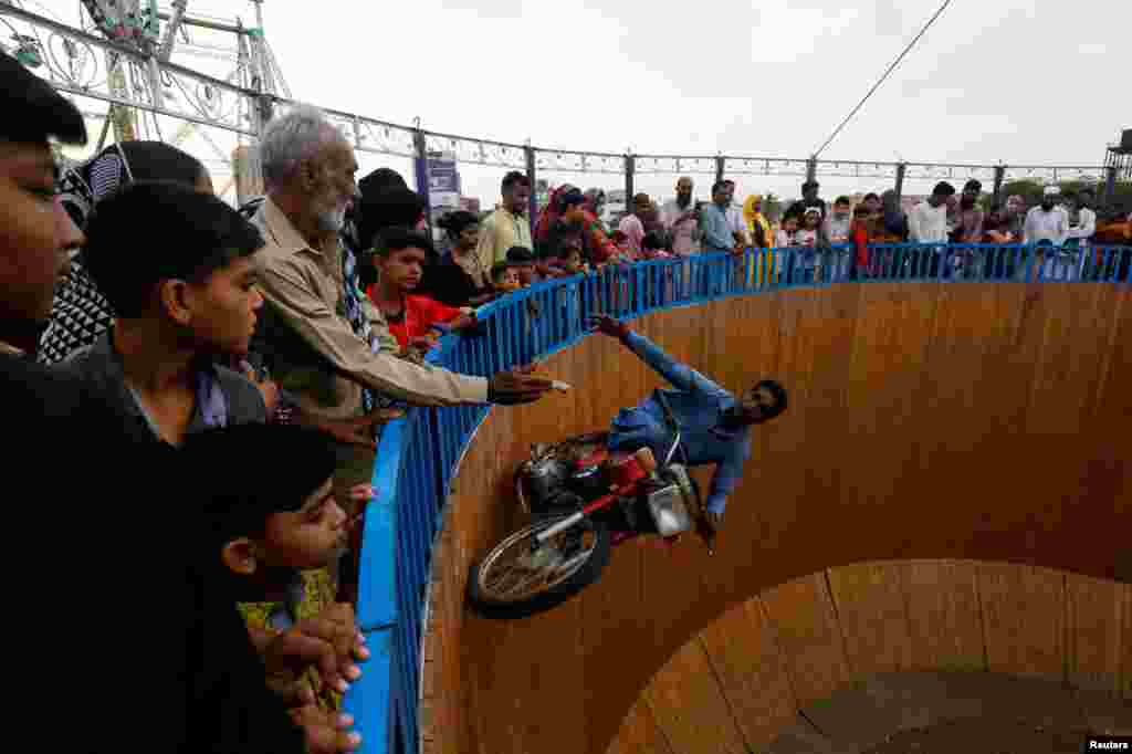 A performer reaches out his hand to get money from the audience, while riding a motorbike with one leg up on the walls of the &quot;Well of Death&quot;, at a fair in Karachi, Pakistan.
