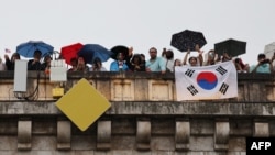 Spectators with a flag of South Korea look on from a Paris bridge to watch the floating parade on the river Seine during the Olympic Games opening ceremony, July 26, 2024.