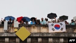 Penonton dengan bendera Korea Selatan menyaksikan parade apung di Sungai Seine dari jembatan Paris selama upacara pembukaan Olimpiade, 26 Juli 2024. (Foto: AFP)