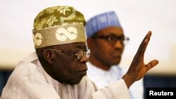 FILE - Bola Tinubu, former Lagos state governor and APC leader, gestures at a party meeting with President-elect Muhammadu Buhari beside him in Abuja, Feb. 17, 2015.