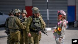 An Israeli activist dressed as a clown salutes a group of Israeli soldiers during a solidarity rally by Israeli left-wing activists in the West Bank town of Hawara.