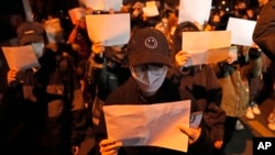 FILE - Protesters hold up blank pieces of paper and chant slogans as they march to protest strict anti-virus measures in Beijing, Nov. 27, 2022.
