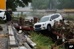 Residents walk near a vehicle washed away by flood waters in the Mentougou district on the outskirts of Beijing, Aug. 1, 2023.