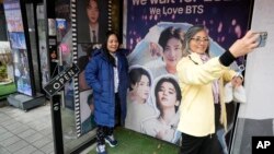 Seorang perempuan berswafoto dengan gambar anggota band K-pop Korea Selatan BTS di depan sebuah kafe di Seoul, Korea Selatan, Senin, 11 Desember 2023. (Foto: AP)