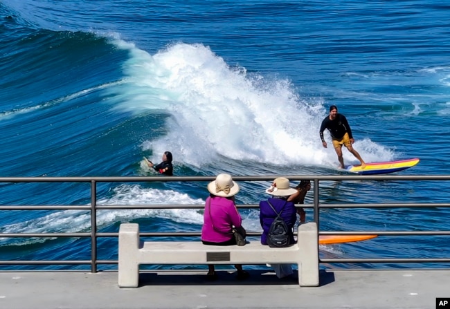 FILE - People watch surfers ride the waves in Huntington Beach, Calif., on Tuesday, Sept. 19, 2023. A California lawmaker is trying to get the state to study how to make people happier. (Jeff Gritchen/The Orange County Register via AP, File)