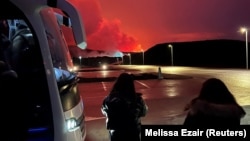 People who are being evacuated stand by a bus as a volcano erupts, in Grindavik, Iceland, March 16, 2024, in this picture obtained from social media.