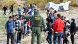 FILE - A U.S. Border Patrol agent directs asylum-seekers waiting between the double fence along the U.S.-Mexico border near Tijuana, Mexico, May 8, 2023, in San Diego, California. 