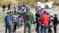FILE - A U.S. Border Patrol agent directs asylum-seekers waiting between the double fence along the U.S.-Mexico border near Tijuana, Mexico, May 8, 2023, in San Diego, California. 