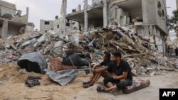 Dua pemuda Palestina duduk di depan sebuah bangunan yang rata setelah serangan udara Israel semalaman di Rafah di Jalur Gaza selatan, pada 9 Oktober 2023. (Foto: AFP)