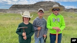 In this image provided by Giant Screen Films, Liam Fisher, Kaiden Madsen and Jessin Fisher pose for a celebratory photo on the day their fossil find was determined to be a juvenile T. rex, in North Dakota. 