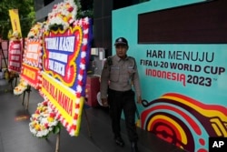 Seorang satpam berjalan di antara spanduk FIFA U-20 World Cup dan karangan bunga ucapan belasungkawa yang dikirim oleh suporter sepak bola, di luar gedung kantor Persatuan Sepak Bola Indonesia (PSSI) di Jakarta. (Foto: AP/Dita Alangkara)