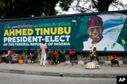 FILE - People sit under a billboard with a congratulatory message of the President-elect Bola Ahmed Tinubu of the All Progressives Congress in Lagos, Nigeria, March 5, 2023.