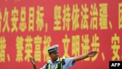 (FILE) A police officer gesturing in front of a propaganda billboard urging "the maintenance of rule of law in Xinjiang" on a road in China's northwestern Xinjiang region, July 19, 2023.