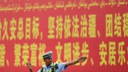 Seorang polisi tampak berdiri di depan papan iklan propaganda yang berbunyi "pemeliharaan aturan hukum di Xinjiang" yang ditulis dalam Bahasa Mandarin dan Uyghur dan terpasang di sebuah jalan di prefektur Kashgar, Xinjiang, pada 19 Juli 2023. (Foto: AFP/Pedro Pardo)
